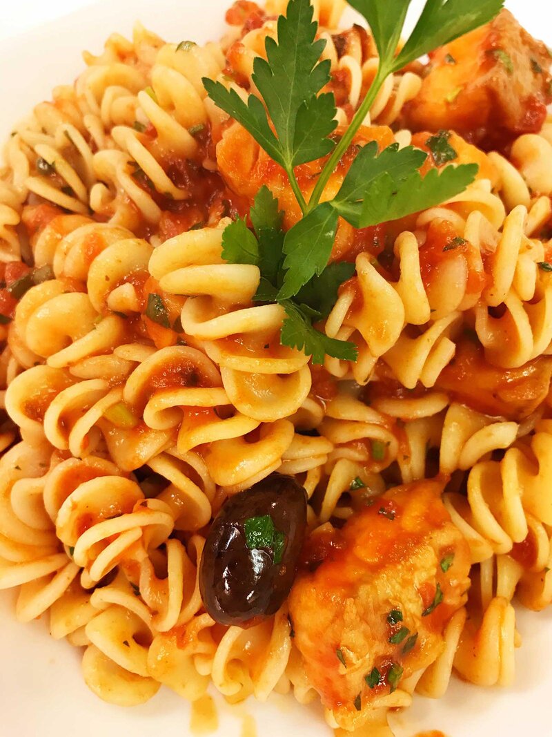 Spiral shaped pasta with olives and marinara sauce topped with basil