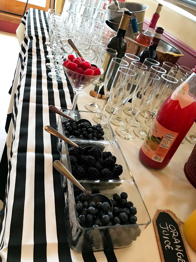 Table with multiple wine and champagne glasses, with bowls filled with berries